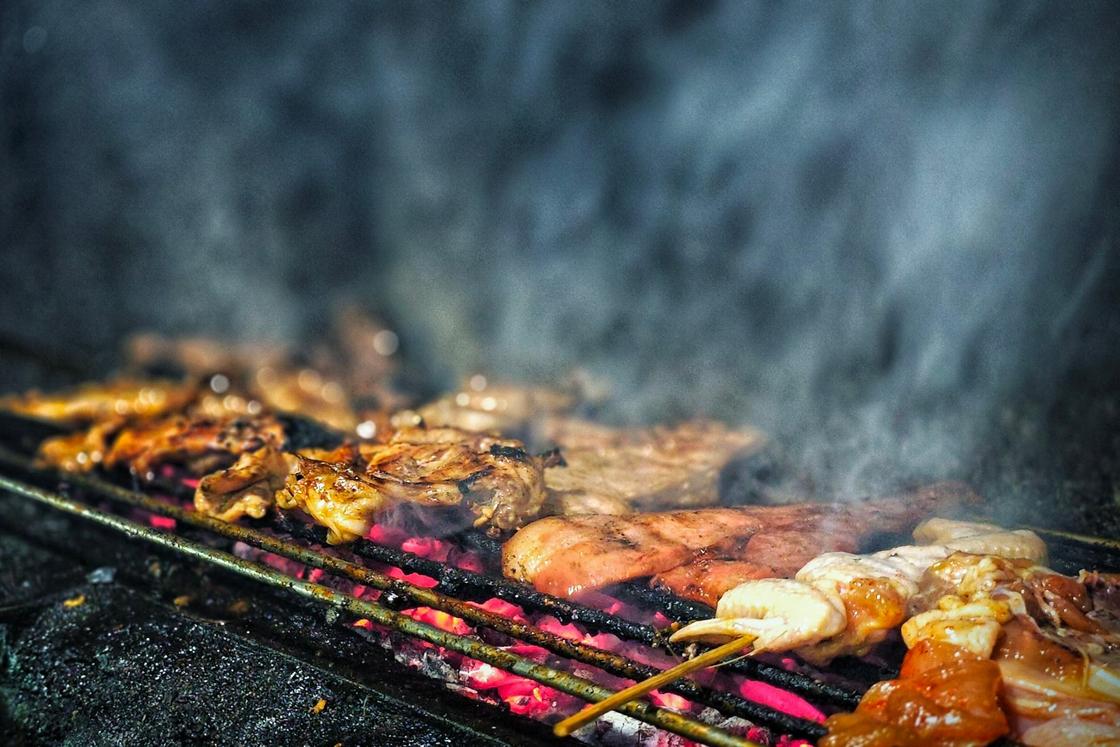 Meat and skewers grilling over glowing charcoal, with smoke rising