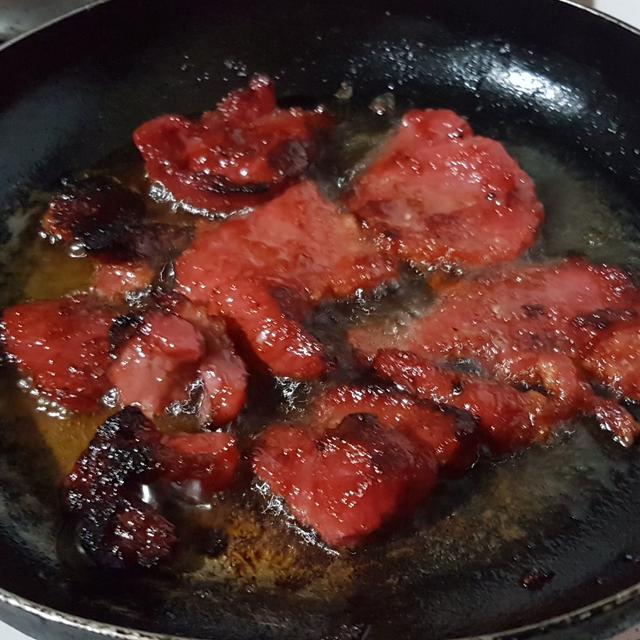 Slices of red cured pork tocino frying in a black pan