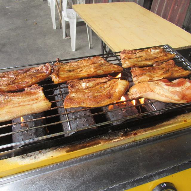Slabs of pork belly cooking on a grill over hot coals