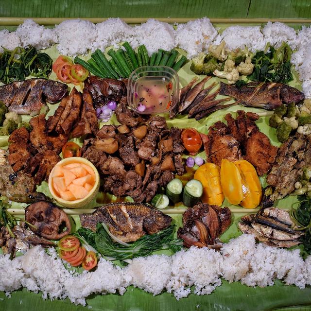 A kamayan spread of rice, grilled fish, meat and vegetables on a banana leaf, seen from above