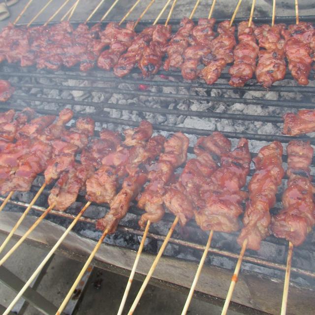 Rows of marinated pork skewers on a smoking charcoal grill