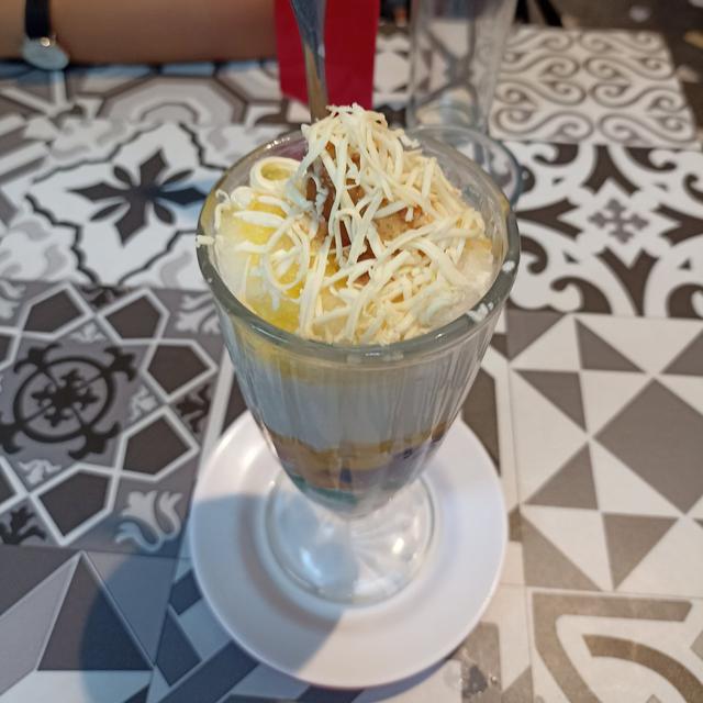 A tall glass of halo-halo topped with grated cheese, on a patterned tile table