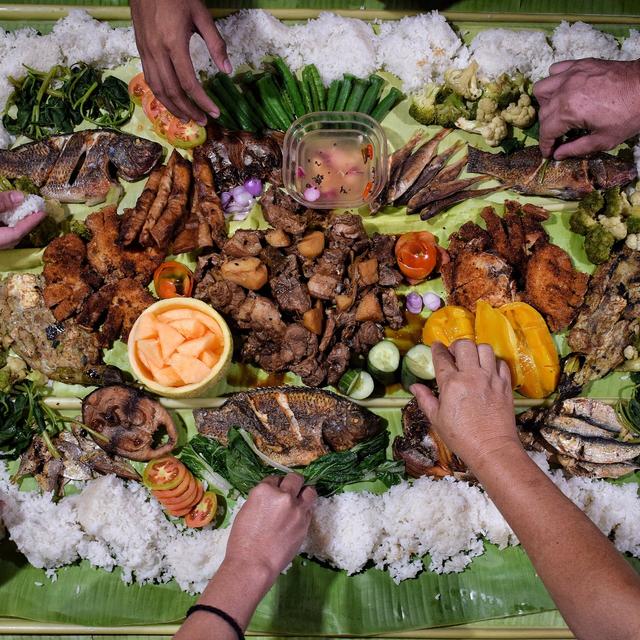 Hands reaching into a kamayan spread on a banana leaf